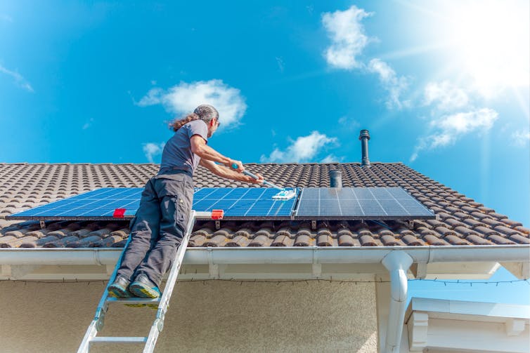 man on ladder holds mop to clean solar panels