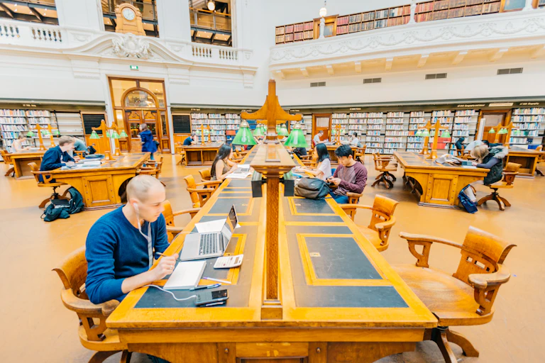 Young people work on laptops and read books in a library.