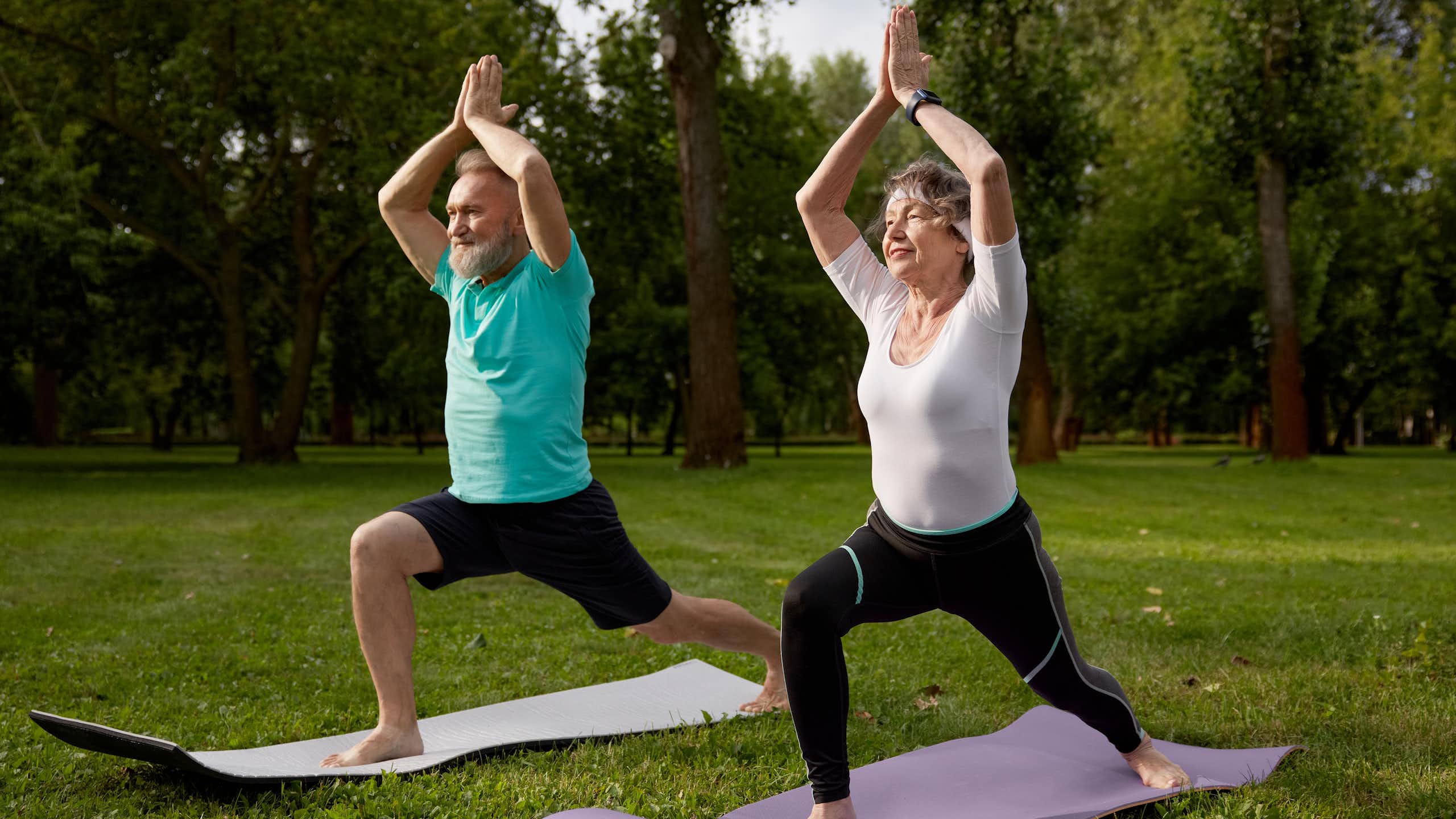 An older man and woman perform the warrior 1 pose.