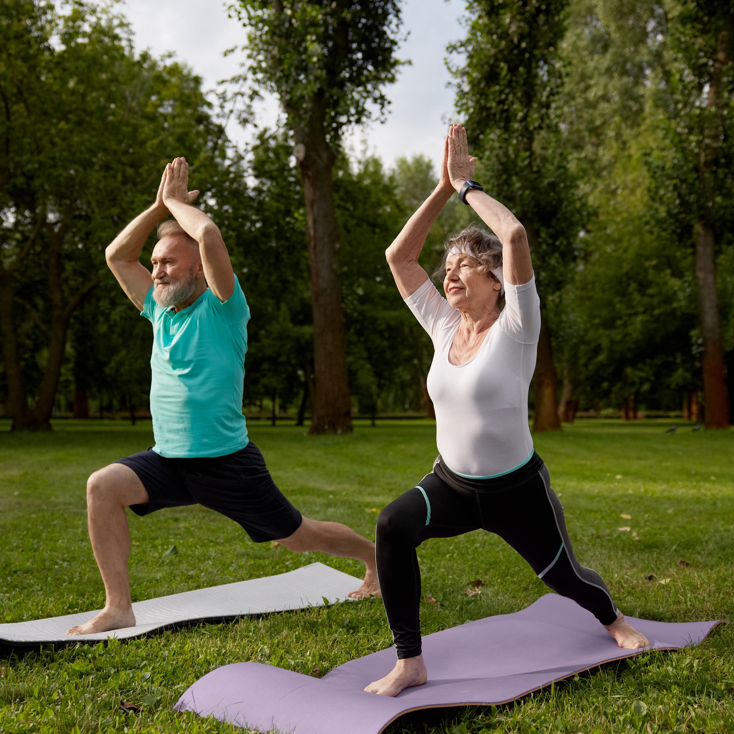 An older man and woman perform the warrior 1 pose.
