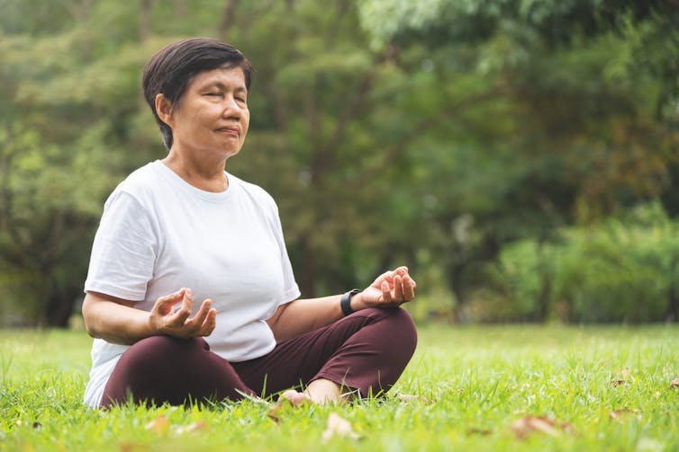 An older woman meditates outdoors.