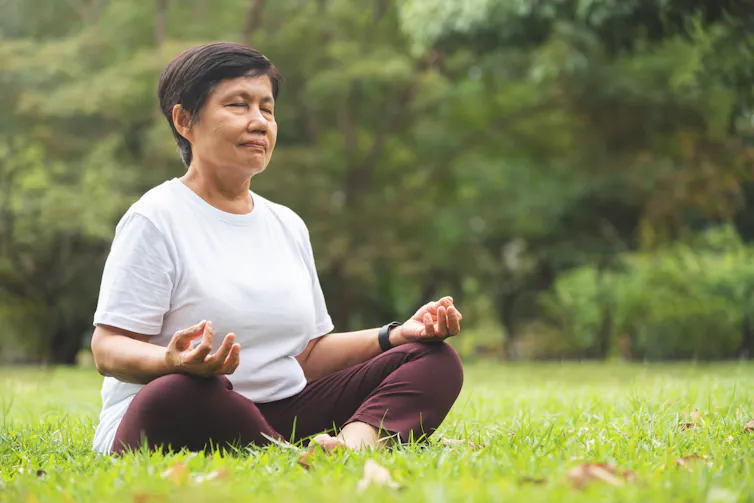 An older woman meditates outdoors.