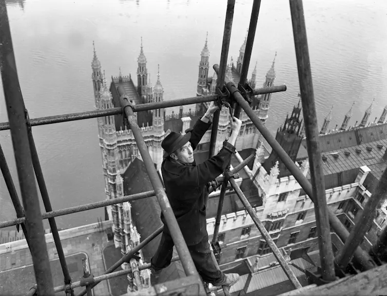 A construction worker stands on scaffolding high up over the Houses of Parliament.