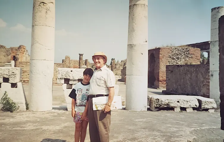 A boy and his grandfather smiling on holiday in front of ancient Roman pillars