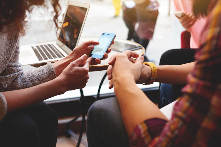 Close up of two women sitting at a cafe, looking at news on their mobile phone