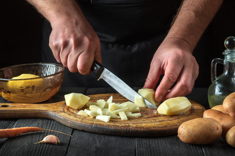 Close up of a chef's hands chopping potatoes to prepare a dish