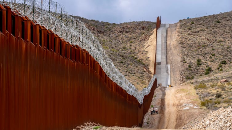 a barbed-wire topped wall running through a desert