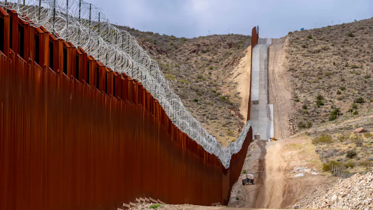 a barbed-wire topped wall running through a desert