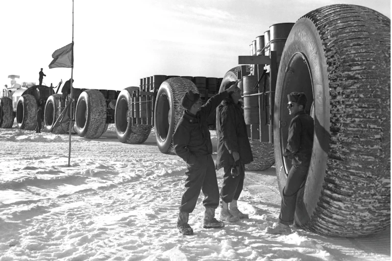 Soldiers stand next to giant wheels on a supply train designed to cross the Greenland ice sheet. An Army “Sno-Train” at Camp Century during construction on the Greenland Ice Sheet in 1959. The tires, four feet wide and ten feet tall, were designed not to sink into soft snow. In the years that followed, the Camp Century ice core, vital to the Army’s mission to understand climate change, was carried off the ice sheet in wagons equipped with the same oversized tires.