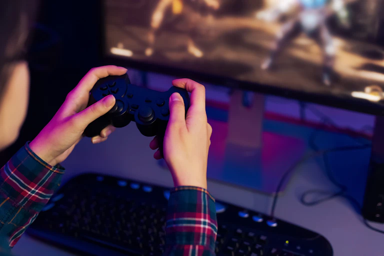 Close up of a pair of hands using a video game controller to play a game that is seen on a computer screen in the background