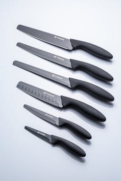 Seis facas de cozinha de ponta redonda de tamanhos variados, alinhadas sobre um fundo branco liso