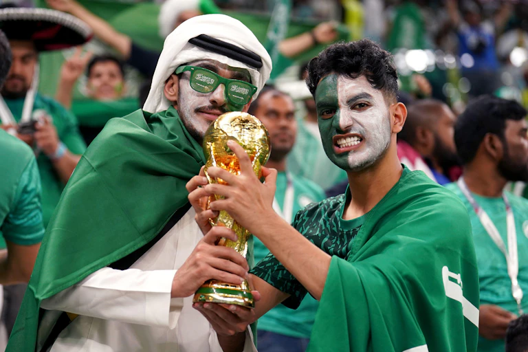 Two fans in green and white hold a replica World Cup trophy.