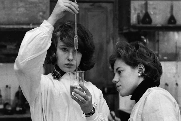 une photo en noir et blanc de deux jeunes filles qui font une expérience de chimie