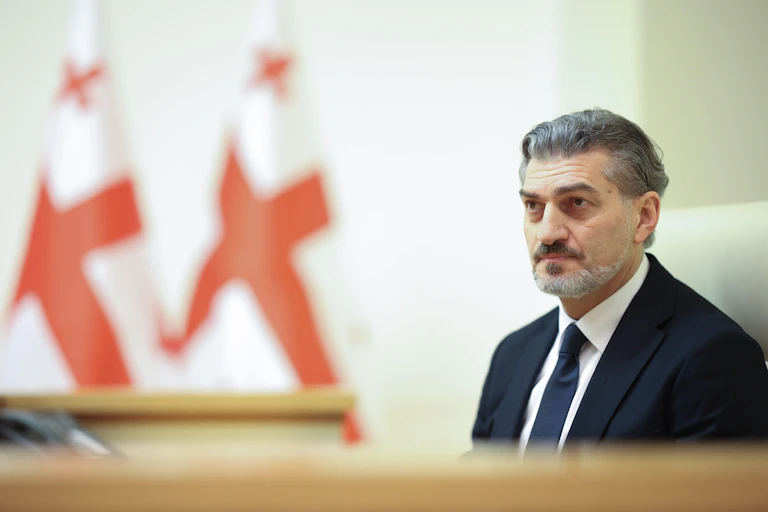 Mikheil Kavelashvili next to two Georgian flags.