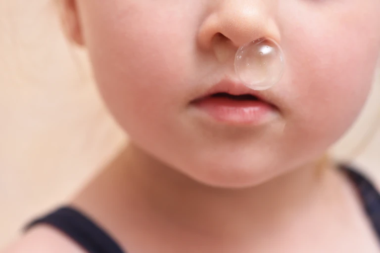 A child blowing a clear snot bubble from their nose.