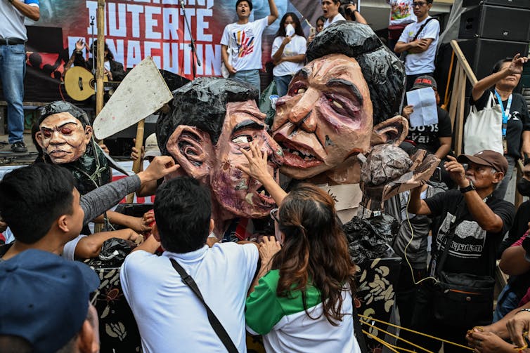 Men and women claw at a large papermache head.