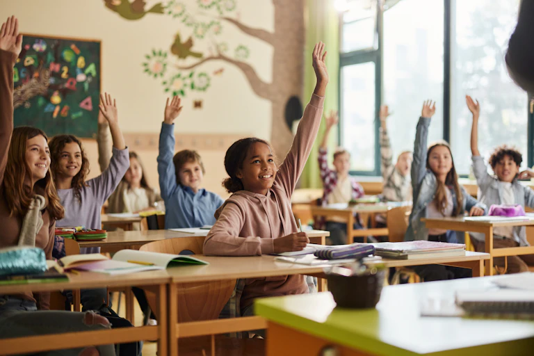 a mix of students sitting in a classroom raise their hands