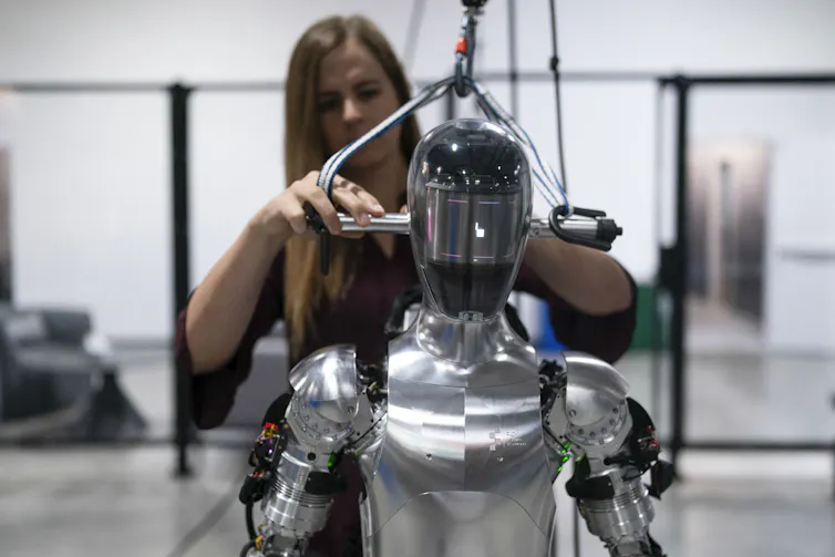 A woman stands next to a robot.