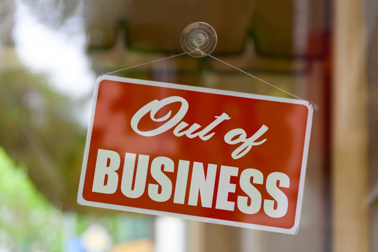 A sign that says 'Out of Business' hanging on the inside of a closed glass door