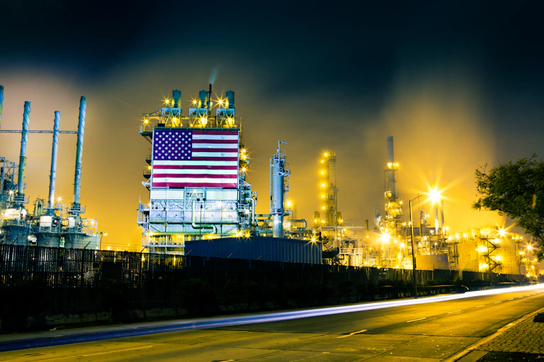 A refinery with a large American flag on the side is lit up at night.