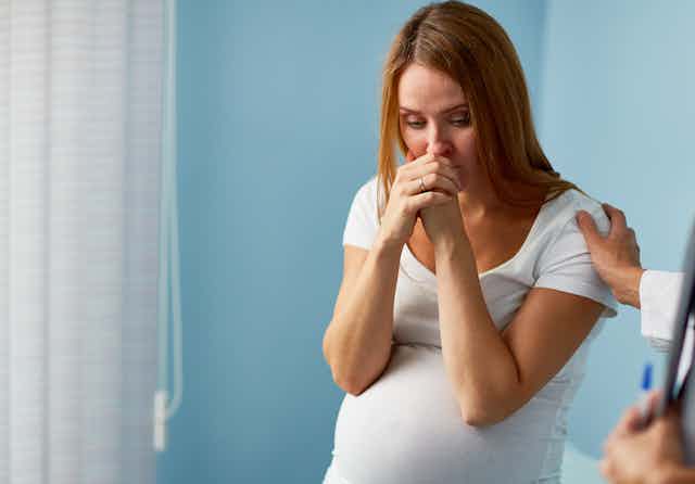 A distraught pregnant woman in a clinical setting with her doctor nearby.