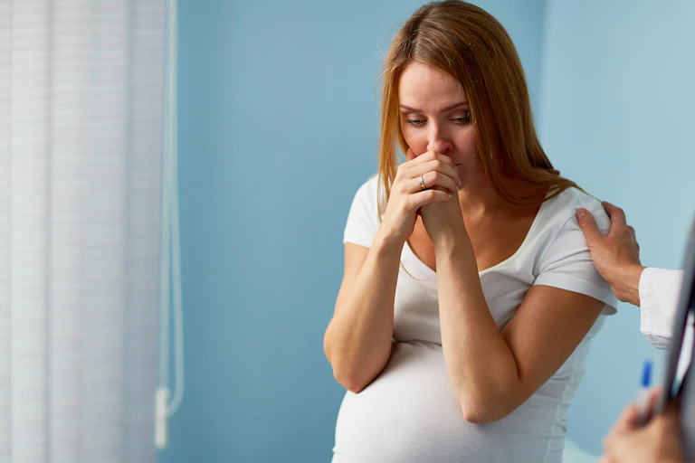 A distraught pregnant woman in a clinical setting with her doctor nearby.