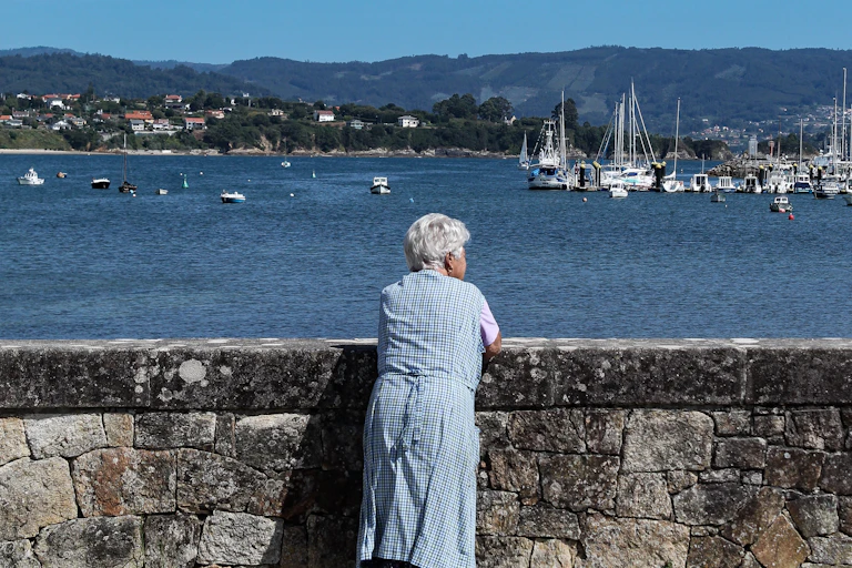 Una mujer en bata mira desde un muro al mar.