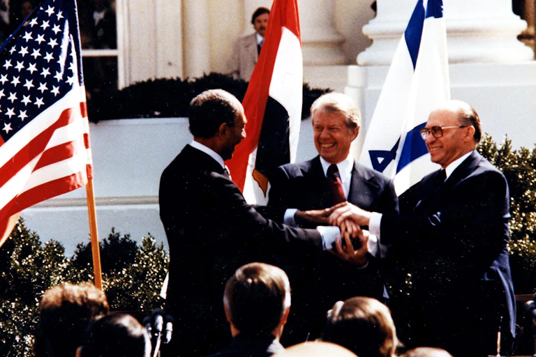 Três homens apertam as mãos em frente à Casa Branca: Anwar El Sadat, Jimmy Carter e Menachem Begin na Casa Branca, para assinar o tratado de paz Egito-Israel de 1979.