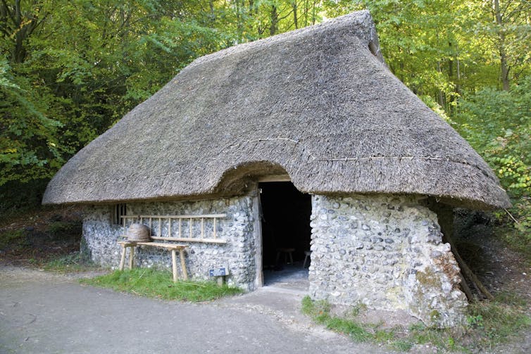A photo of a primitive stone house with a thatched roof.