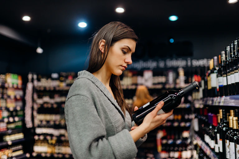 Une femme regarde l'étiquette d'une bouteille de vin dans un supermarché