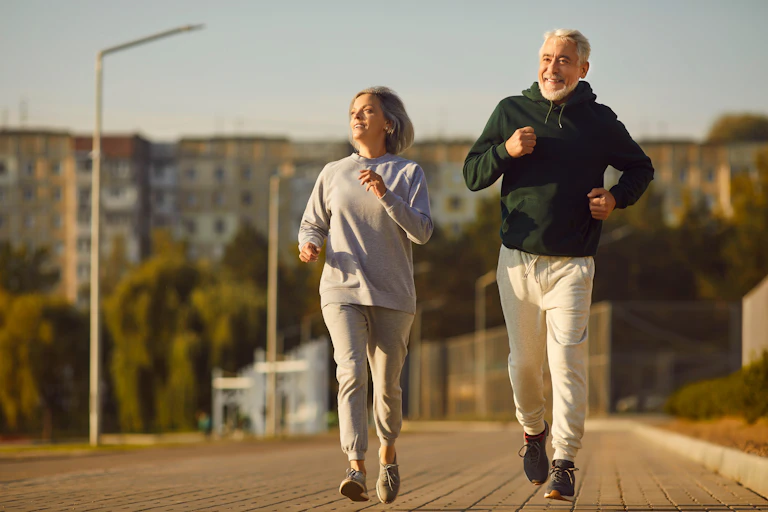 Um casal de idosos sai para correr ao ar livre em um dia ensolarado.