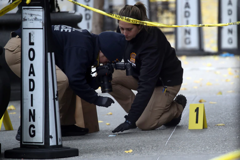Two police officers are seen hunching over concrete, documenting evidence at the site of the shooting.
