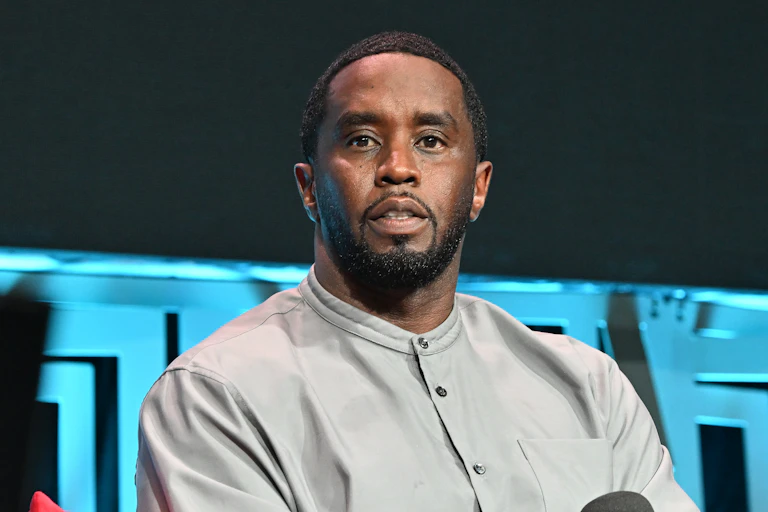 A Black man with facial hair is seen looking beyond the camera.