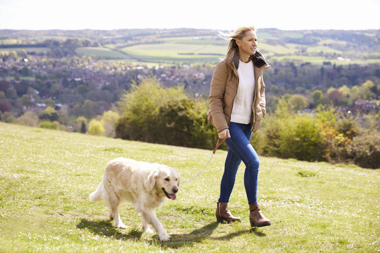 A woman wearing a jacket walks her dog outdoors.