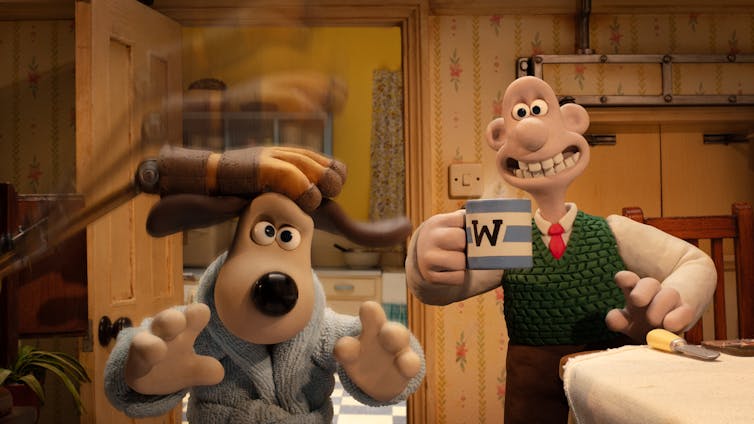 Wallace drinking tea and watching Gromit being patted by a robot hand.