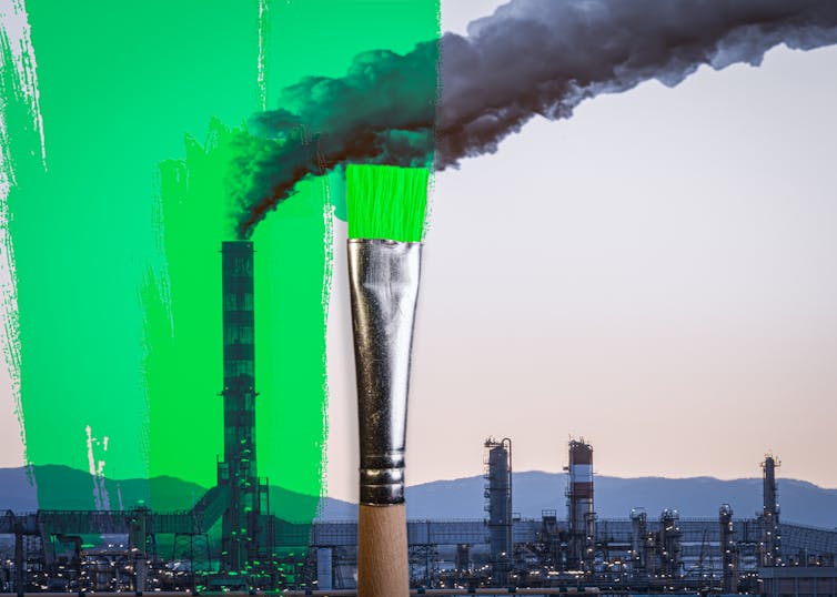 A brush spreading green paint on a photo of a city skyline that includes a chimney bellowing smoke