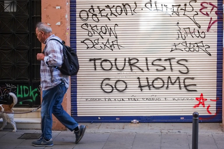 A man walks past a shop shutter with graffiti..