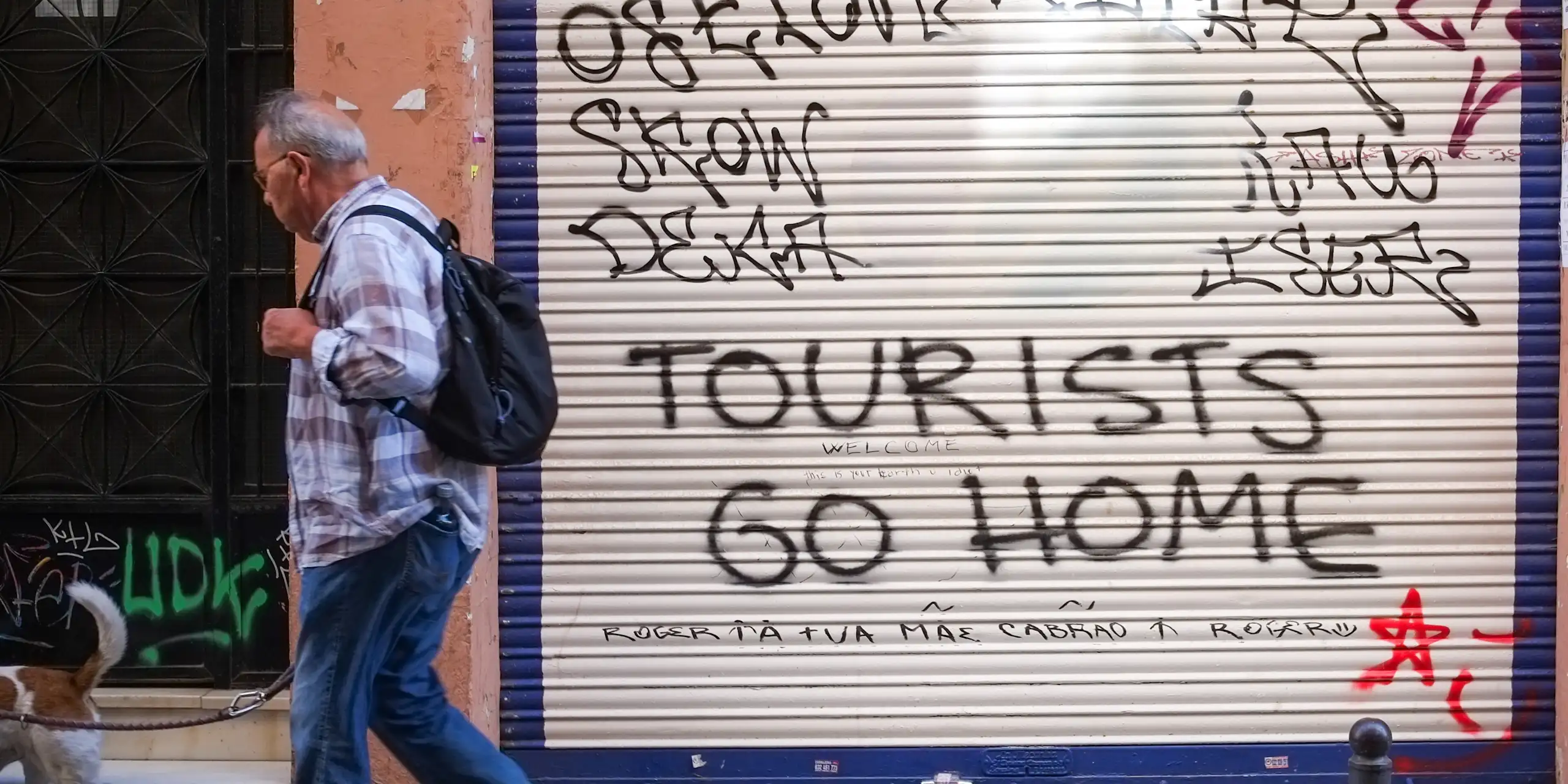 A man walks past a shop shutter with graffiti..