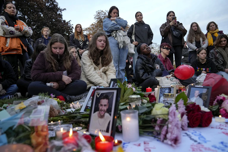 A group of young women stand and kneel next to a vigil with candles and photos of liam payne