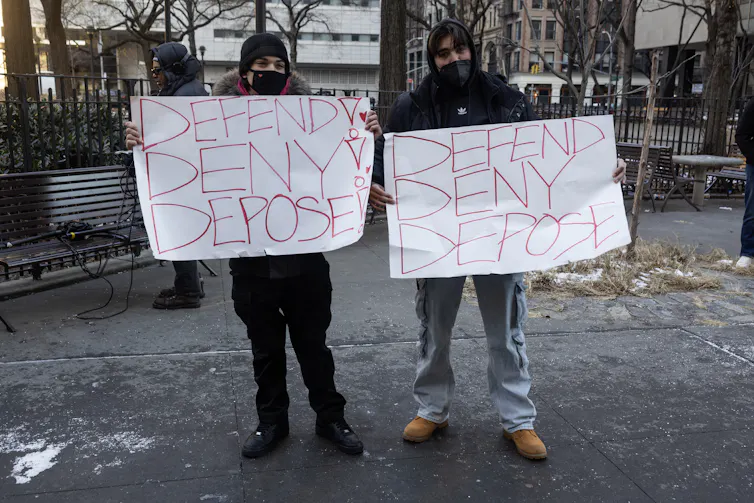 Two young men hold handmade signs that read