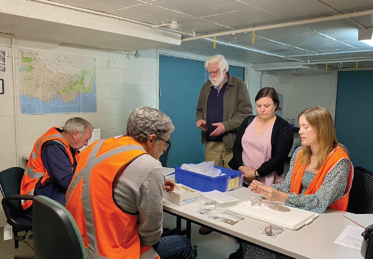 Group of people standing around a table looking at stone artefacts.