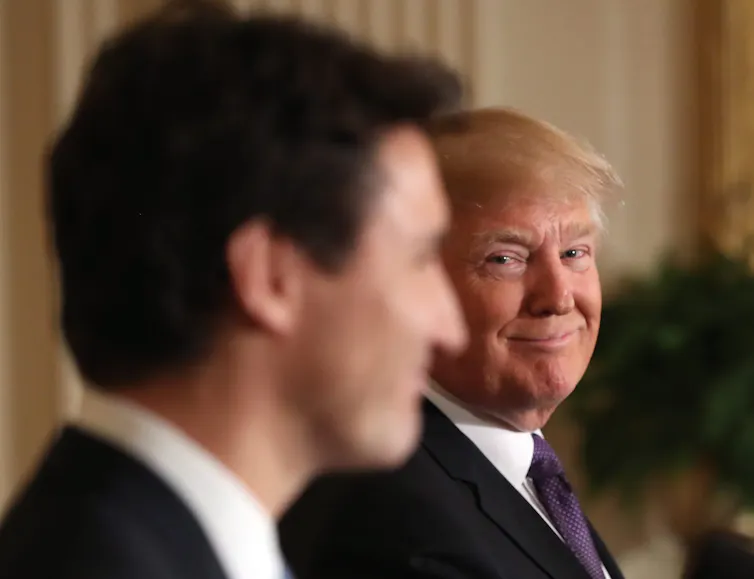 A man with orange-ish blond hair smiles over at a younger man with dark hair seen in silhouette.