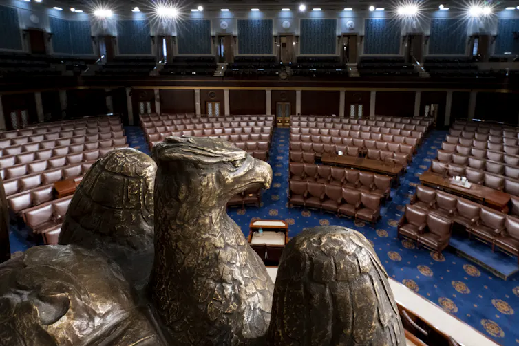 L’hémicycle de la Chambre des représentants, avec un aigle sculpté dans la pierre au premier plan et des rangées de sièges à l’arrière-plan