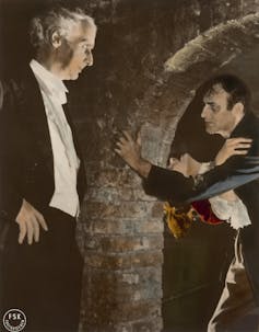 Un hombre mayor en frac observa a otro que abraza a una mujer.