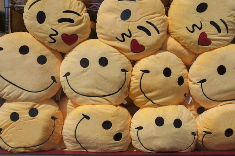 yellow cushions with smiley faces are stacked on top of each other, with a few kiss faces on top