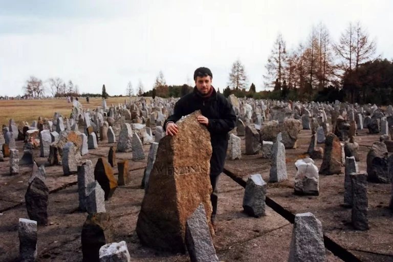 A man stands behind a field of gravestones.