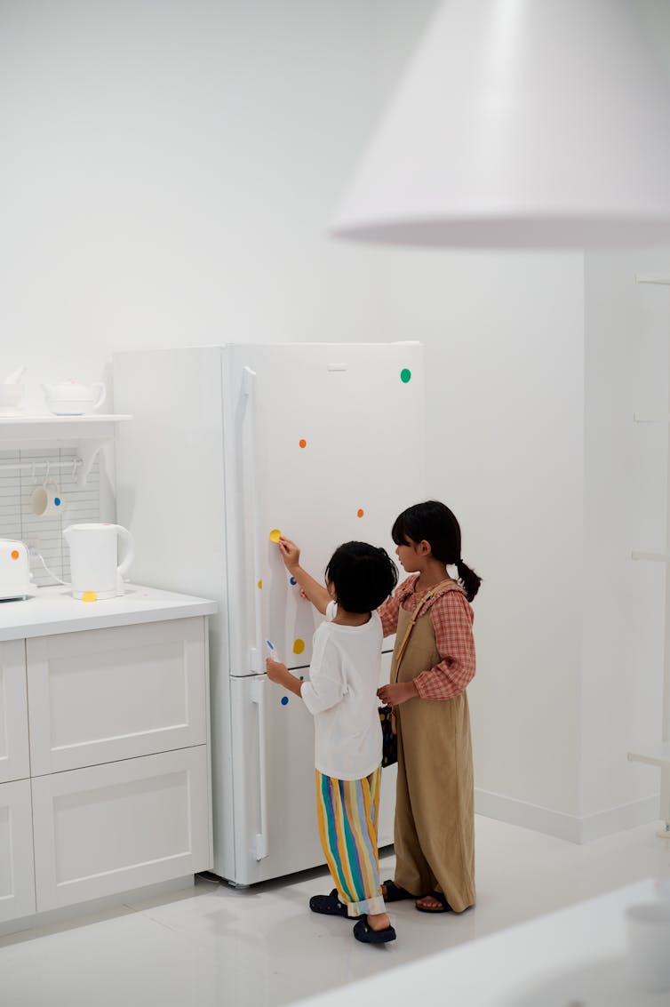 Children in a white room, sticking colourful dots on a fridge.