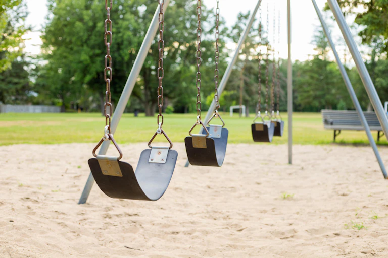 Several empty black swings on a playground in a grassy park.