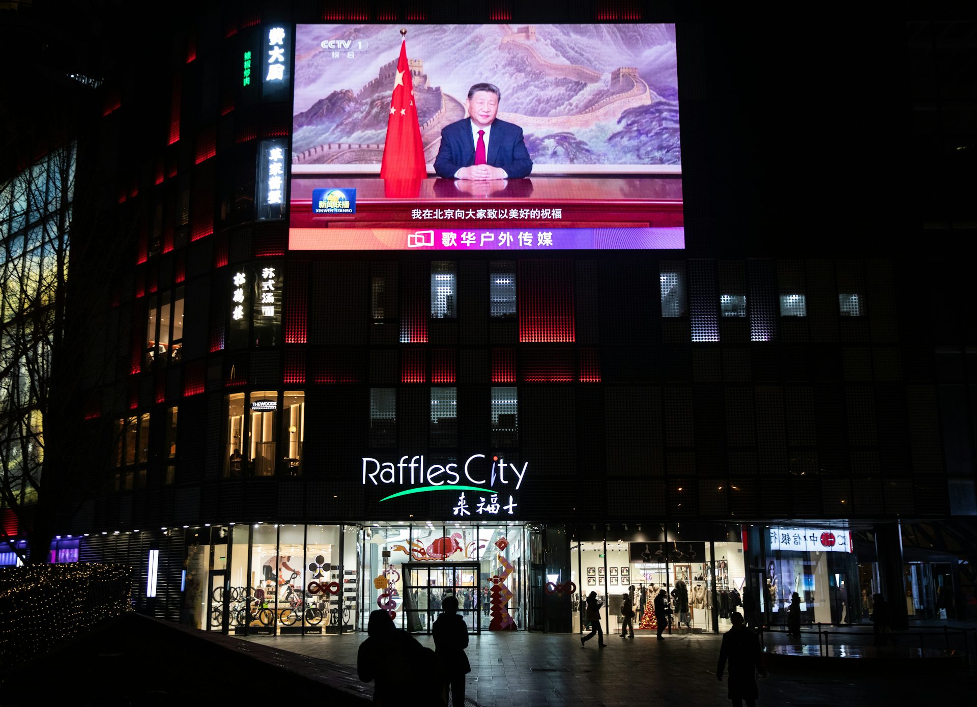 People walk past a screen showing Xi's televised address.