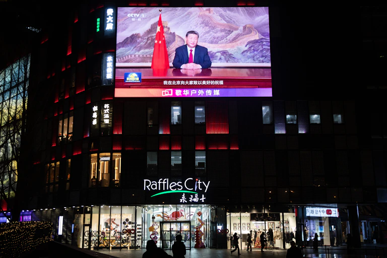 People walk past a screen showing Xi's televised address.